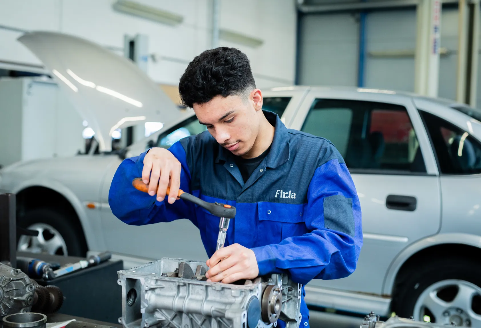 Student technisch specialist personenauto's sleutelt aan motorblok van een auto bij Firda Heerenveen