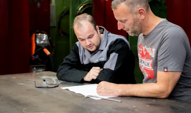 Twee mannen aan een tafel bij een technische tekening