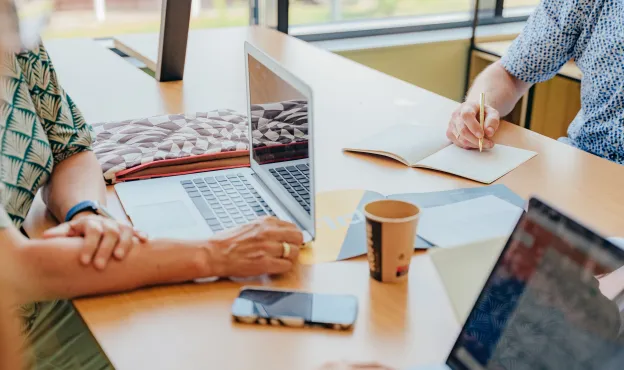 de handen van drie mensen aan een tafel met laptops
