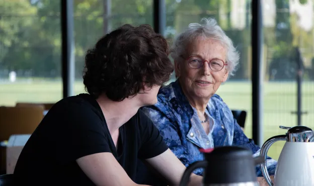 oudere vrouw aan tafel met zorgmedewerker