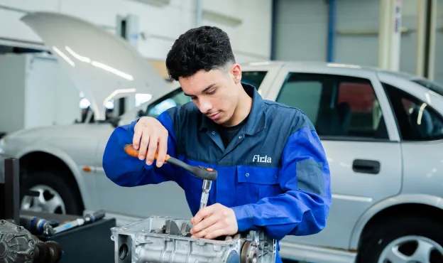 Student technisch specialist personenauto's sleutelt aan motorblok van een auto bij Firda Heerenveen